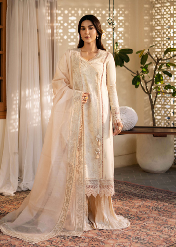 Woman in a beige traditional outfit standing in a decorated room with plants and a table.