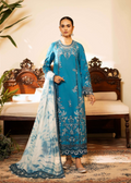 Woman in a blue embroidered traditional outfit standing in a decorated room with wooden furniture and plants.