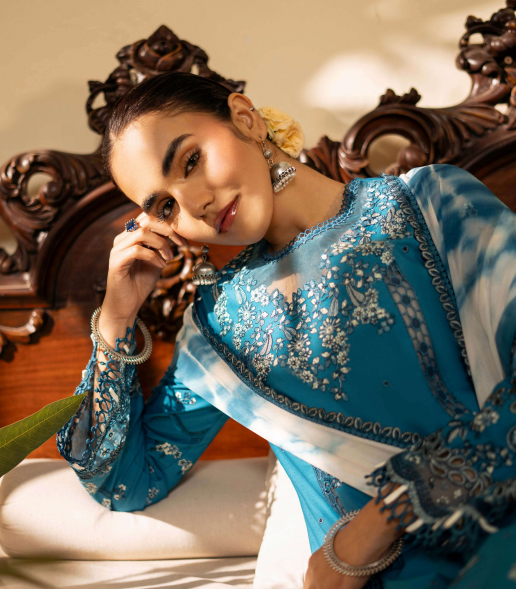 Woman in a blue embroidered traditional outfit sitting on a decorative chair.