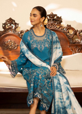 Woman in a blue and white embroidered traditional outfit sitting on an ornate wooden chair.