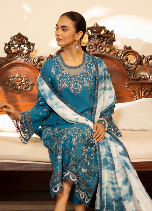 Woman in a blue and white embroidered traditional outfit sitting on an ornate wooden chair.