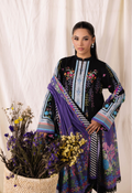 Woman wearing a black outfit with colorful floral patterns, holding a purple scarf, against a white curtain background.