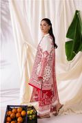 Woman wearing a red and white embroidered traditional outfit with a white curtain and green plant in the background.