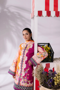 Woman in a colorful traditional outfit standing next to a table with fruits and flowers.
