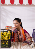 Woman in a colorful scarf standing in front of a fruit stand with a white background