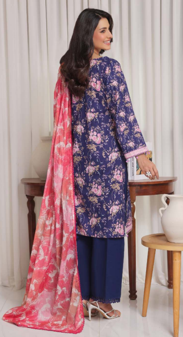Woman wearing a blue floral dress with a pink dupatta in a room setting.