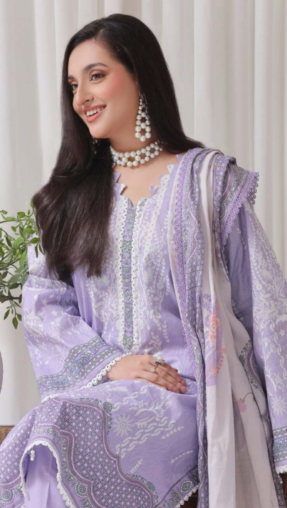 Woman wearing a light purple embroidered traditional outfit with a white dupatta against a white curtain background.
