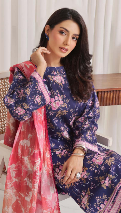 Woman wearing a blue floral dress with a pink dupatta, sitting on a chair.