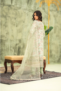 Woman in a light green floral dress with a sheer dupatta against a textured wall.
