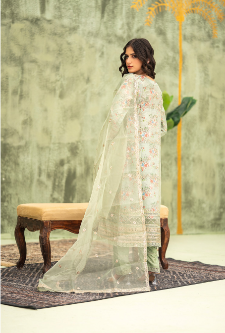 Woman in a light green floral dress with a sheer dupatta against a textured wall.