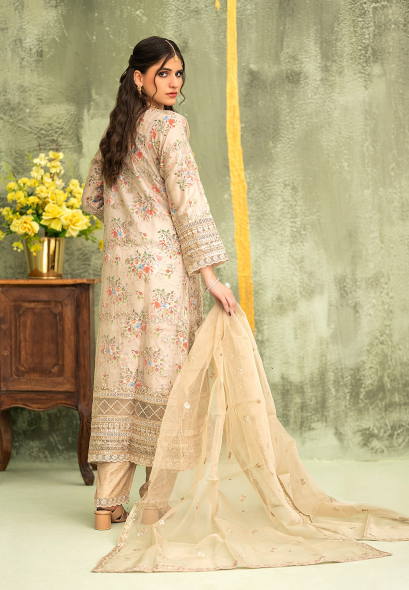Woman in a traditional outfit with a floral design, standing against a textured wall with a wooden table and flowers.