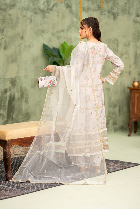 Woman in a white traditional outfit with a sheer dupatta, holding a clutch, against a green wall.