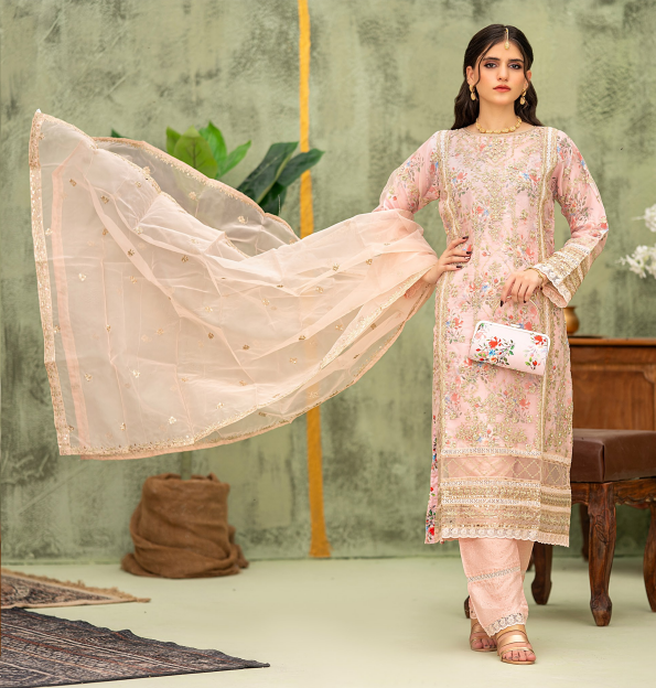 Woman in a pink embroidered outfit holding a matching dupatta in a decorated room.