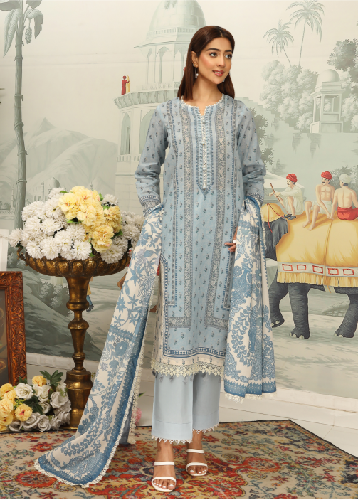 Woman in a light blue embroidered outfit standing in a decorated room with floral arrangements and classical architecture.