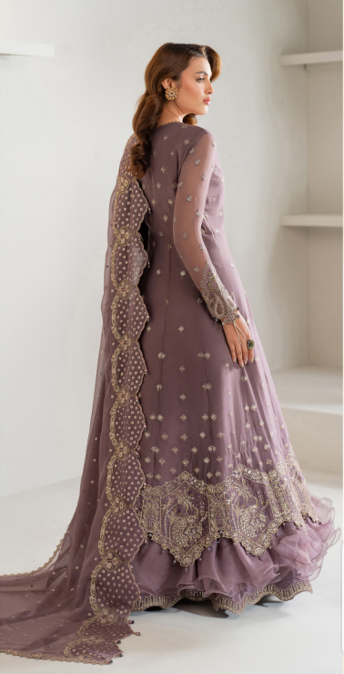 Woman wearing a purple embroidered traditional outfit in a minimal white room.