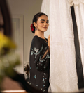 Woman wearing a black dress with floral embroidery standing in a room.
