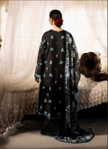 Person wearing a black dress with floral patterns in a room with white curtains.