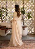 Woman in a beige saree standing in a decorated room with plants and a lattice wall.