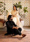 Man and woman sitting on a patterned rug with decorative plants and lattice wall in the background