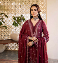 Woman in a burgundy embroidered dress standing in a decorative indoor setting.