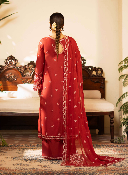 Person wearing a red traditional outfit with white patterns in a room with a wooden bed and decorative elements.