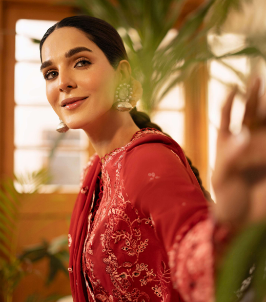 Woman in a red embroidered outfit standing indoors with plants in the background