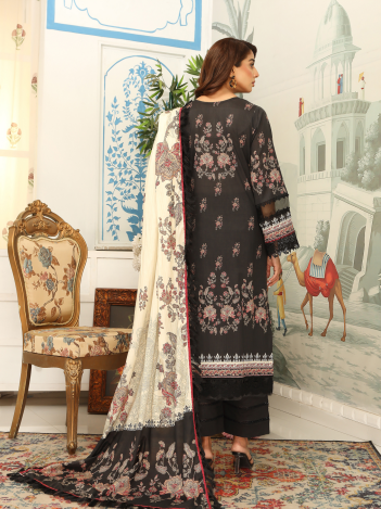 Woman in a black and white embroidered outfit standing in a decorated room with a chair and artwork.