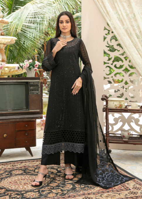 Woman in a black traditional outfit standing in a decorated room with a fountain and decorative wall.