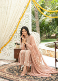 Woman in a traditional outfit sitting on a decorative rug with floral decorations and greenery in the background.
