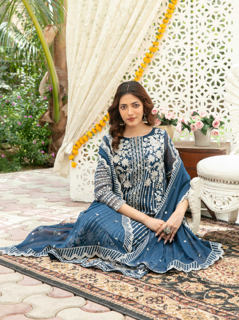 Woman in a blue and white traditional outfit sitting on a patterned rug outdoors.