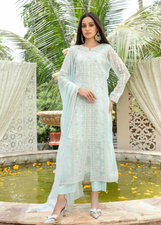 Woman in a light blue traditional outfit standing by a pond with greenery in the background