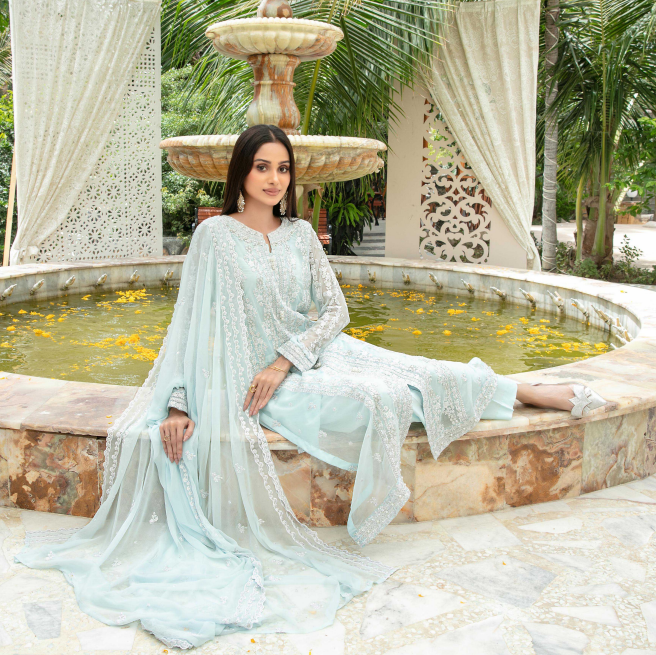 Woman in a light blue traditional outfit sitting by a fountain with greenery in the background
