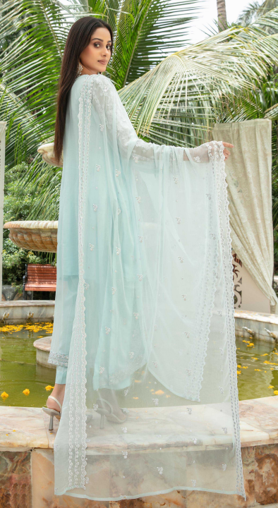 Woman in a light blue traditional outfit standing outdoors with greenery in the background