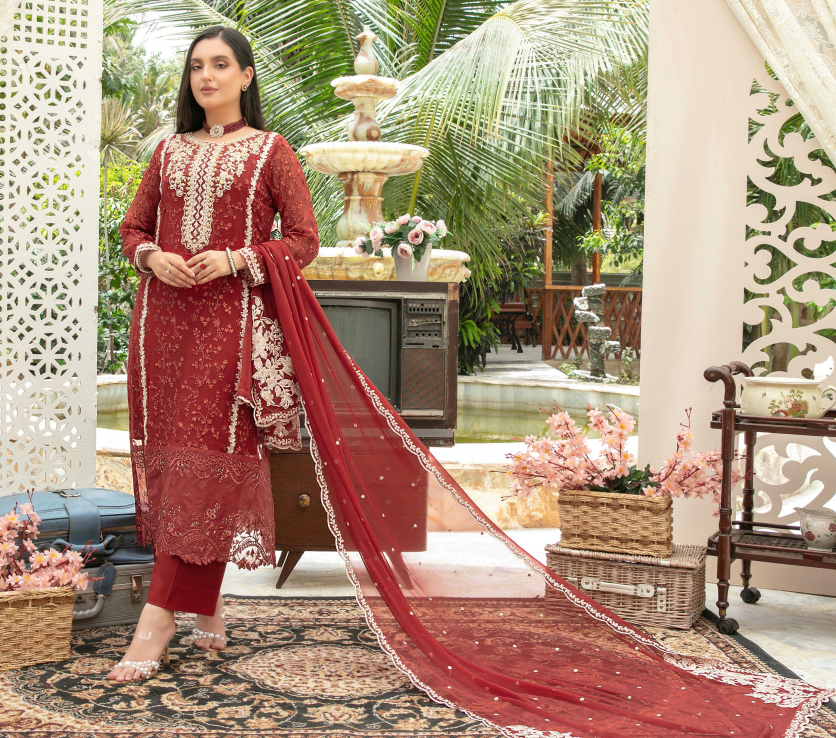 Woman in a red embroidered traditional outfit standing in an outdoor setting with a fountain and greenery.
