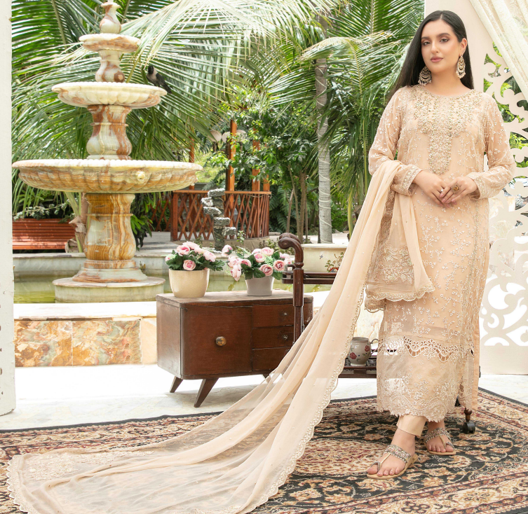 Woman in a beige traditional outfit standing in a garden with a fountain and palm trees.