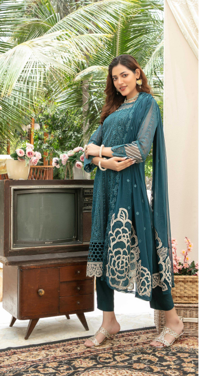 Woman in a teal traditional outfit standing in a room with a vintage television and decorative items.
