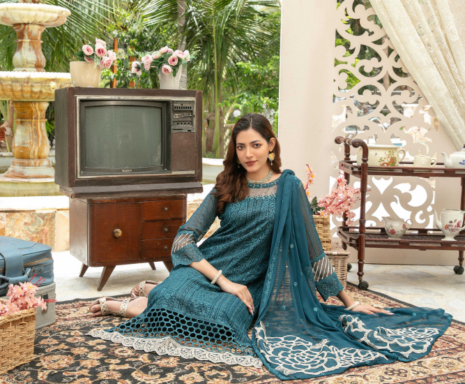 Woman in a blue traditional outfit sitting in a decorated room with vintage furniture and decor.