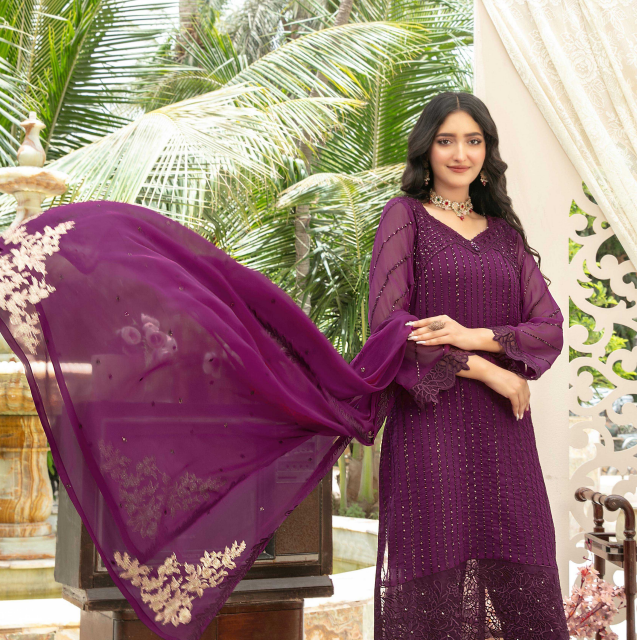 Woman in a purple traditional outfit with a matching dupatta, standing outdoors.