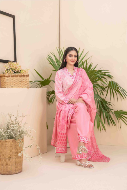 Woman in a pink saree sitting indoors with plants and a basket in the background