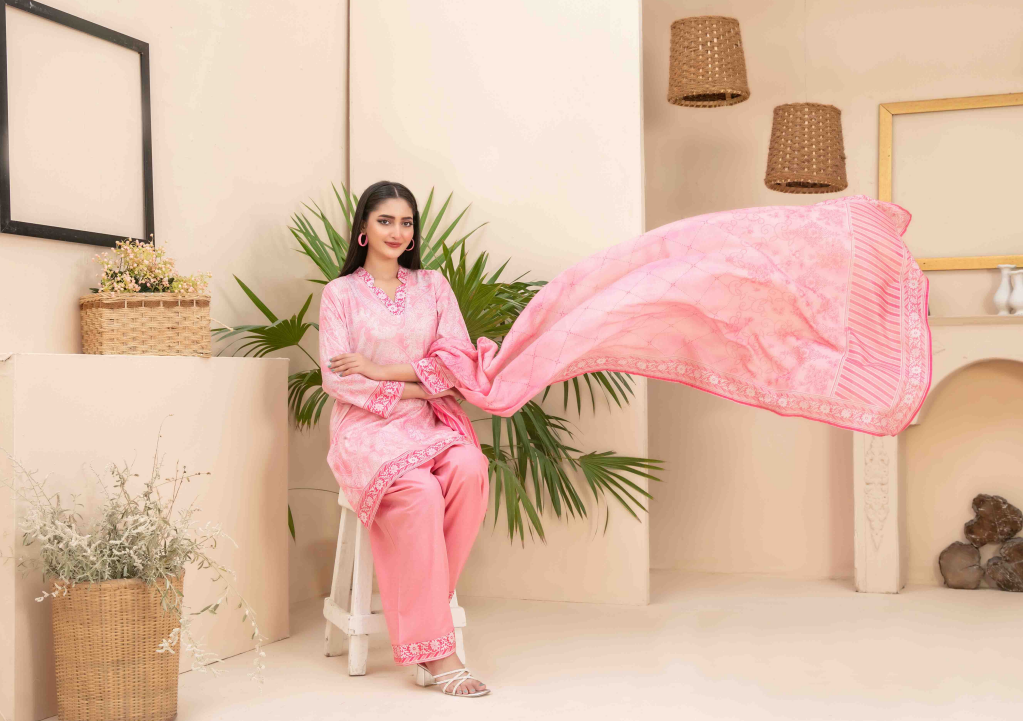 Woman in a pink traditional outfit holding a pink scarf in a home setting.