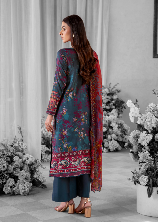Woman wearing a floral embroidered shawl over a blue outfit with flowers and a gray curtain in the background.