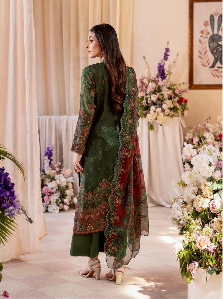 Woman in a green and red traditional outfit standing in a decorated room with flowers.