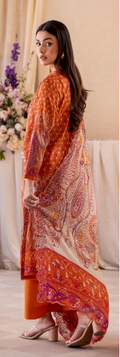 Woman wearing an orange and red patterned outfit with a matching shawl indoors.