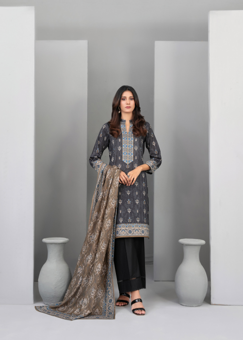 Woman wearing a traditional outfit with a gray and black patterned top and black pants, standing in a minimalistic room.