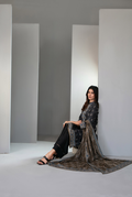 Woman in a black patterned outfit sitting in a minimalistic room with white walls and gray floor.