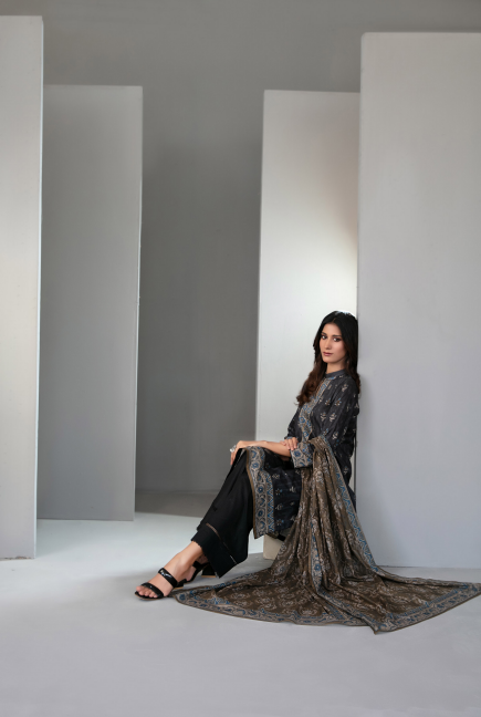 Woman in a black patterned outfit sitting in a minimalistic room with white walls and gray floor.