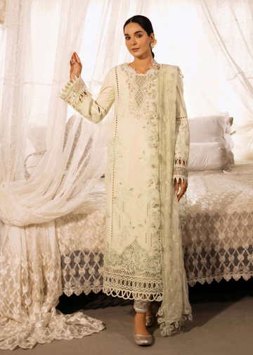 Woman in a light green embroidered traditional outfit standing in a decorated room with white curtains and furniture.