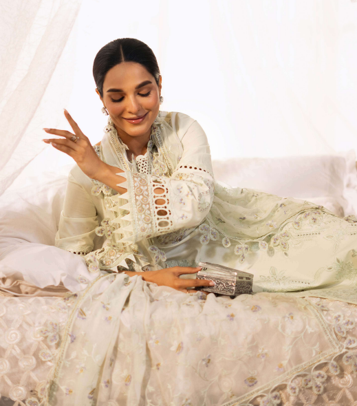 Woman in a white embroidered outfit sitting on a white couch with a white background