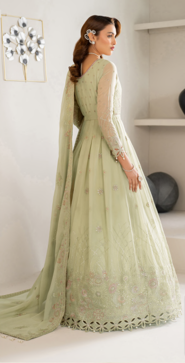 Woman in a light green traditional outfit with floral patterns in a minimalistic room.