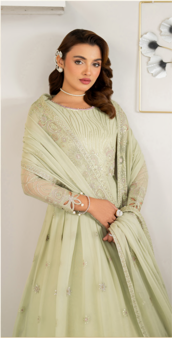 Woman wearing a light green traditional outfit with a matching dupatta against a white wall.